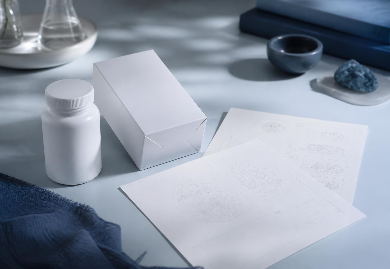 An unlabelled white supplement bottle and blank carton beside marked-up draft artwork sheets — illustrative imagery
